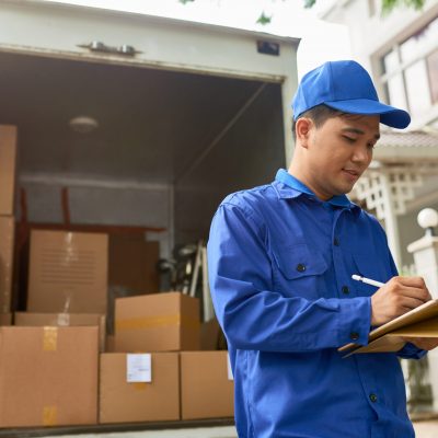 Moving house company courier s Vietnamese moving house company courier standing at delivery truck full of boxes and filling information in contract